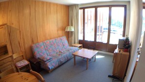 A cozy room with a wooden wall, a sofa, a table, a chair, and a small desk with a lamp. - Charming 2-Room Cabin Apt, 40m², Sleeps 4, Near Vars Les Claux Slopes (Vars)