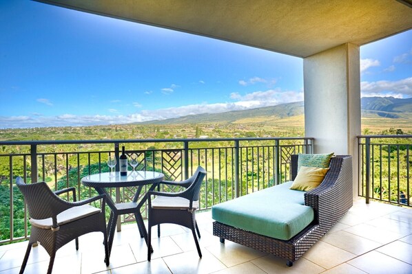 Un balcon avec une table et des chaises, un canapé et une vue sur un paysage verdoyant, avec des montagnes à l’horizon.