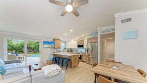 Una cocina moderna con una isla central, un comedor con mesa de madera y una sala de estar con sofá y televisor.