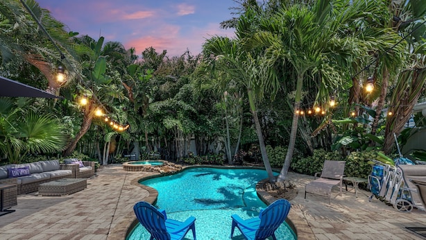 Un área de piscina con una piscina circular, sillas azules y un espacio de lounge con sofás y una mesa.
