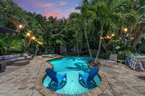 Un área de piscina con una piscina circular, sillas azules y un espacio de lounge con sofás y una mesa.