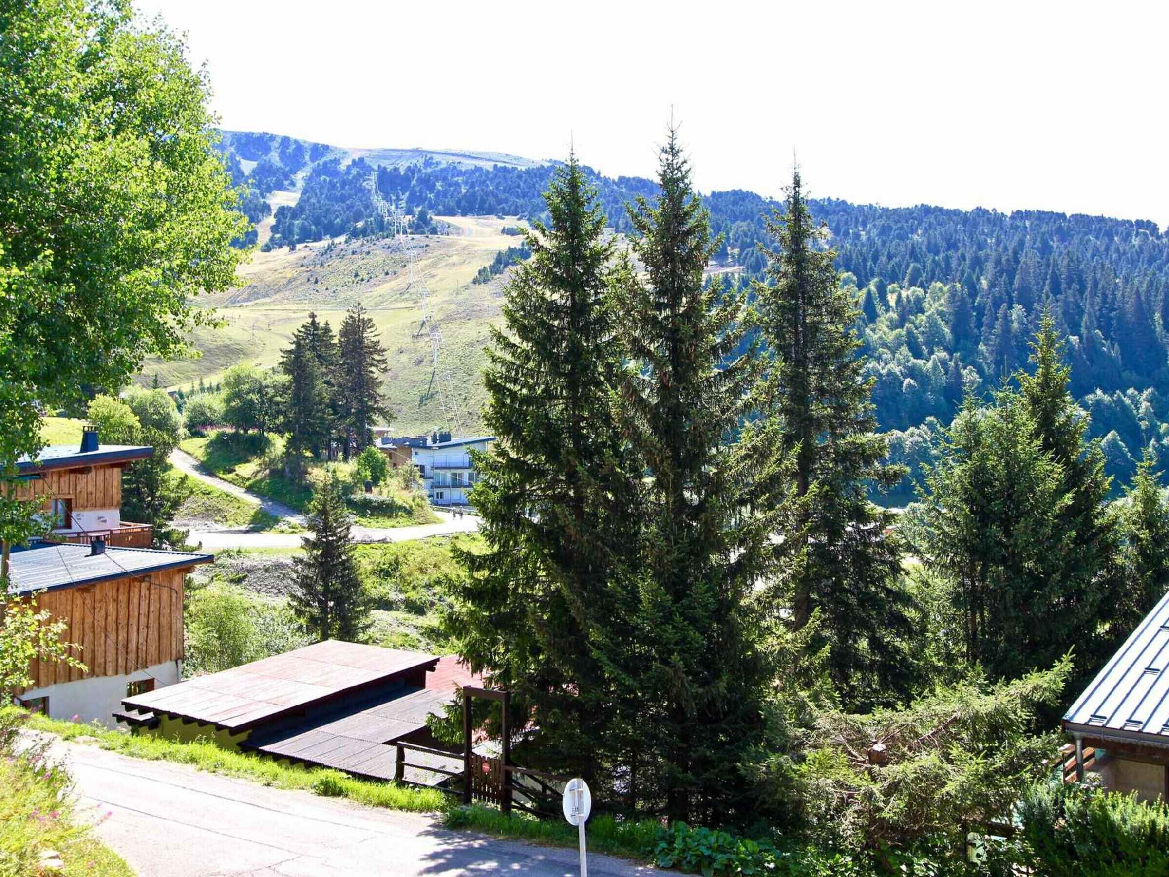A rural setting with a wooden cabin and a modern building, surrounded by dense forest and hills.