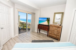 Un dormitorio con una cama grande, televisión, cómoda de madera y balcón con vista a la playa y al océano.