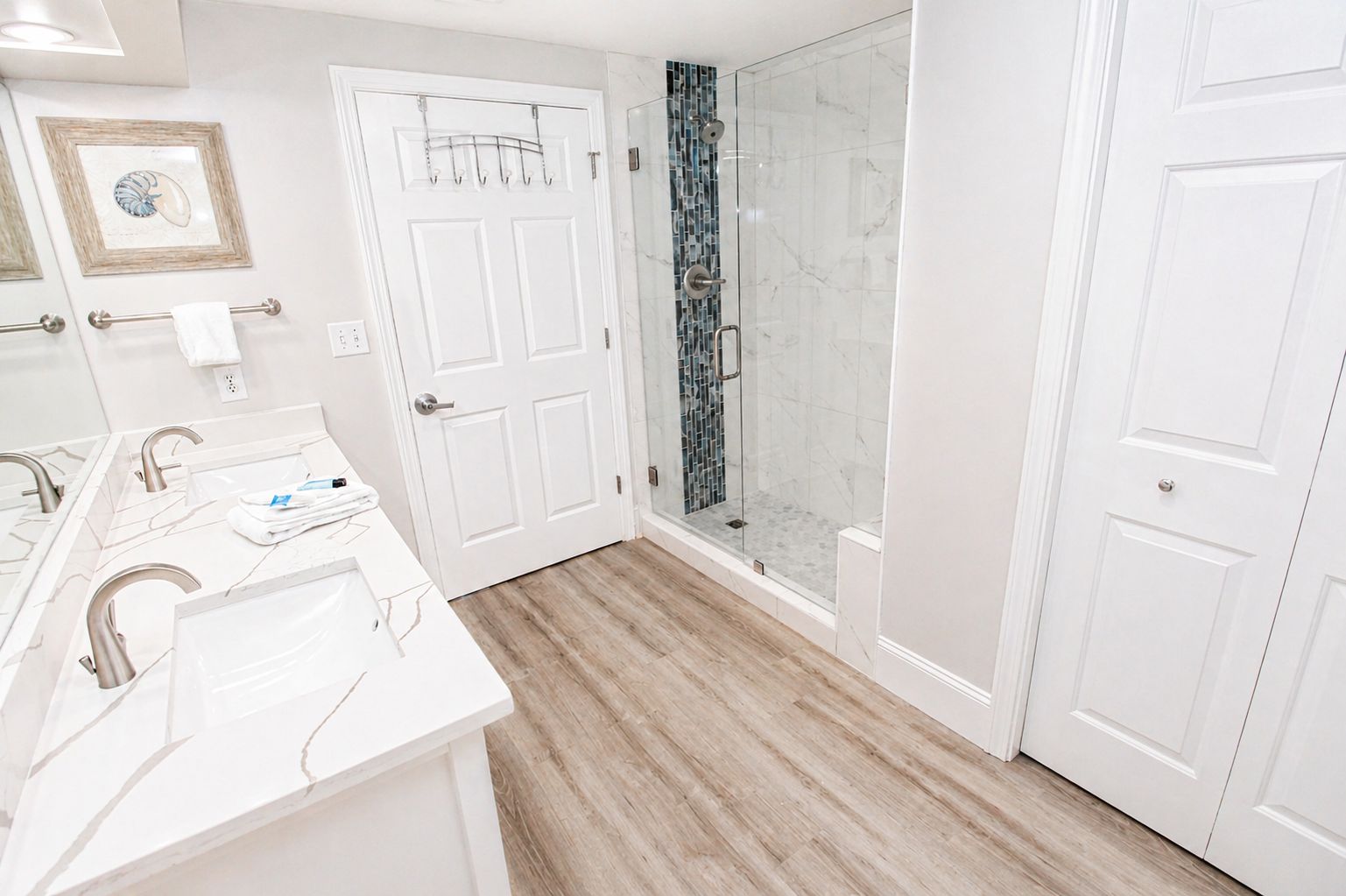A bathroom with a white vanity, a glass shower enclosure, and a wooden floor.