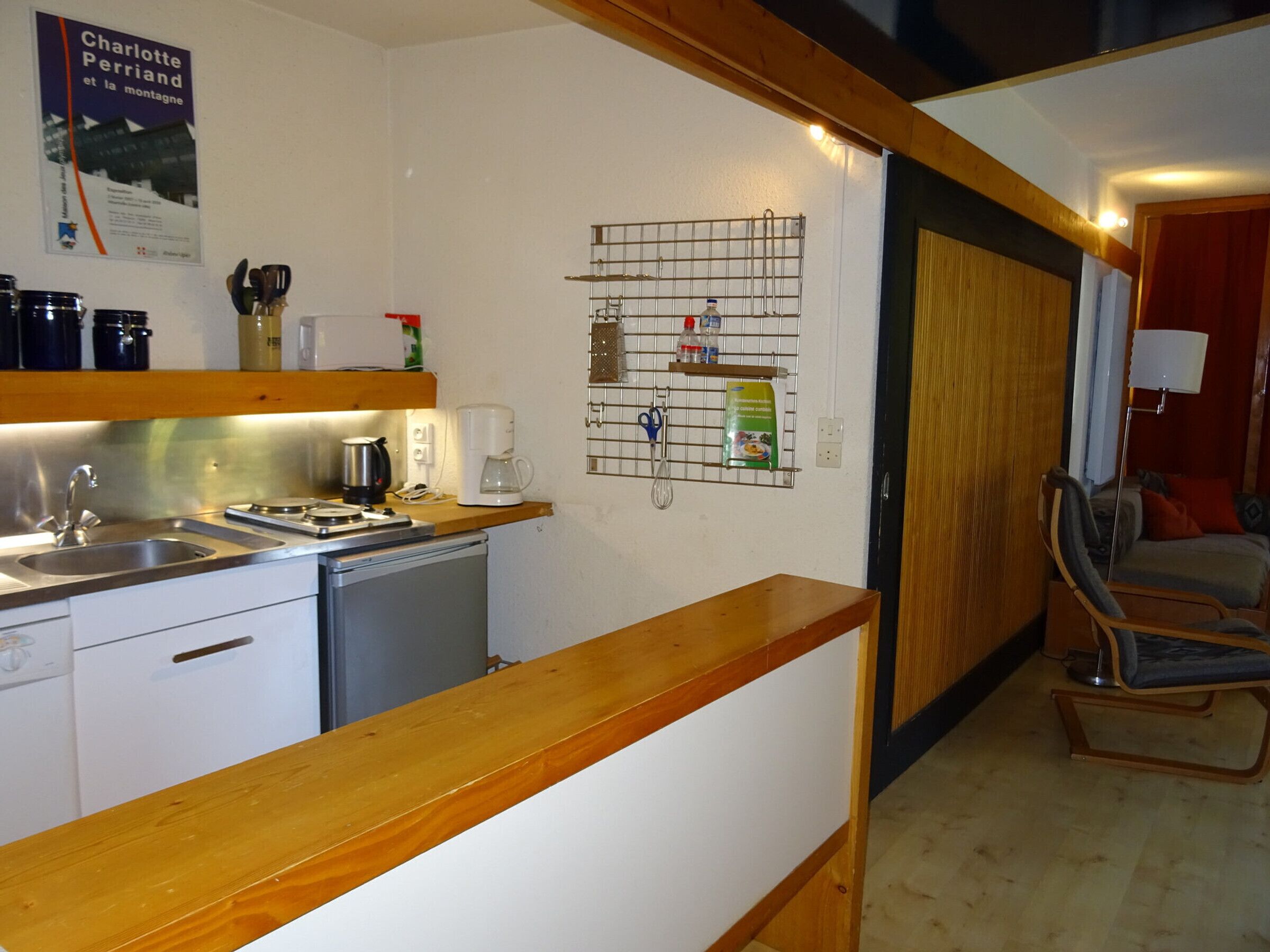 A compact kitchen with a dishwasher, coffee maker, and a metal rack with kitchen utensils.