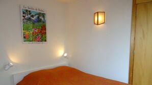 Quarto com cama, luminária na parede e um cartaz de um jardim.