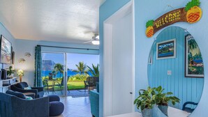 A room with a view of the ocean, a sliding glass door, a blue wall with a welcome sign, and a small plant on the counter.