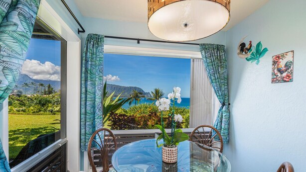 A dining area with a glass table, chairs, and a view of the ocean and mountains.