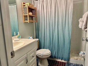 A bathroom with a white sink, a toilet, a shower with a blue curtain, and a small wooden shelf above the sink. - Fountain Head 8 - Condo 2 Bedroom / 2 Bath , maximum occupancy of 6 people. Holmes Beach Anna Maria Island (Holmes Beach)