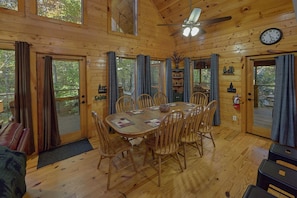 A cabin with a wooden interior, a dining table with chairs, a ceiling fan, and a clock on the wall.