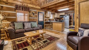 Un intérieur de chalet chaleureux, avec un revêtement mural en bois, un salon doté d’un canapé et d’une table basse, une cuisine équipée d’un réfrigérateur et de tabourets de bar, et un balcon agrémenté d’une rambarde.