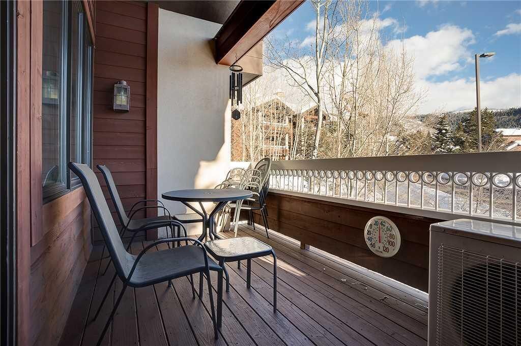 A wooden deck with a table and chairs, a railing, and a thermostat.
