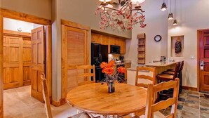 Un'area pranzo con un tavolo e sedie in legno, un vaso con fiori e una cucina sullo sfondo.