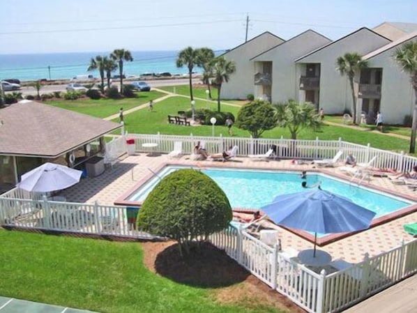 A pool area with a fenced deck, lounge chairs, and umbrellas.