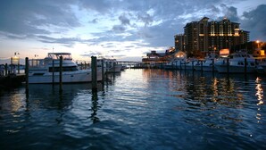 A marina with several yachts docked, a large hotel building in the background, and calm water reflecting the sky. - Blue Surf 12A- 1bd townhome with community pool! (Miramar Beach)