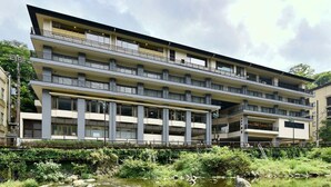 A multi-story building with balconies, a river in front, and a bridge. - Hakoneji Kaiun (Hakone)
