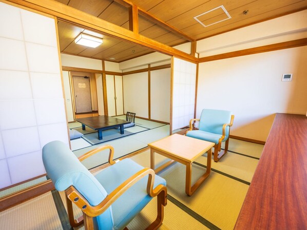 A traditional tatami mat room with a low table, two blue cushioned chairs, and a wooden bench.