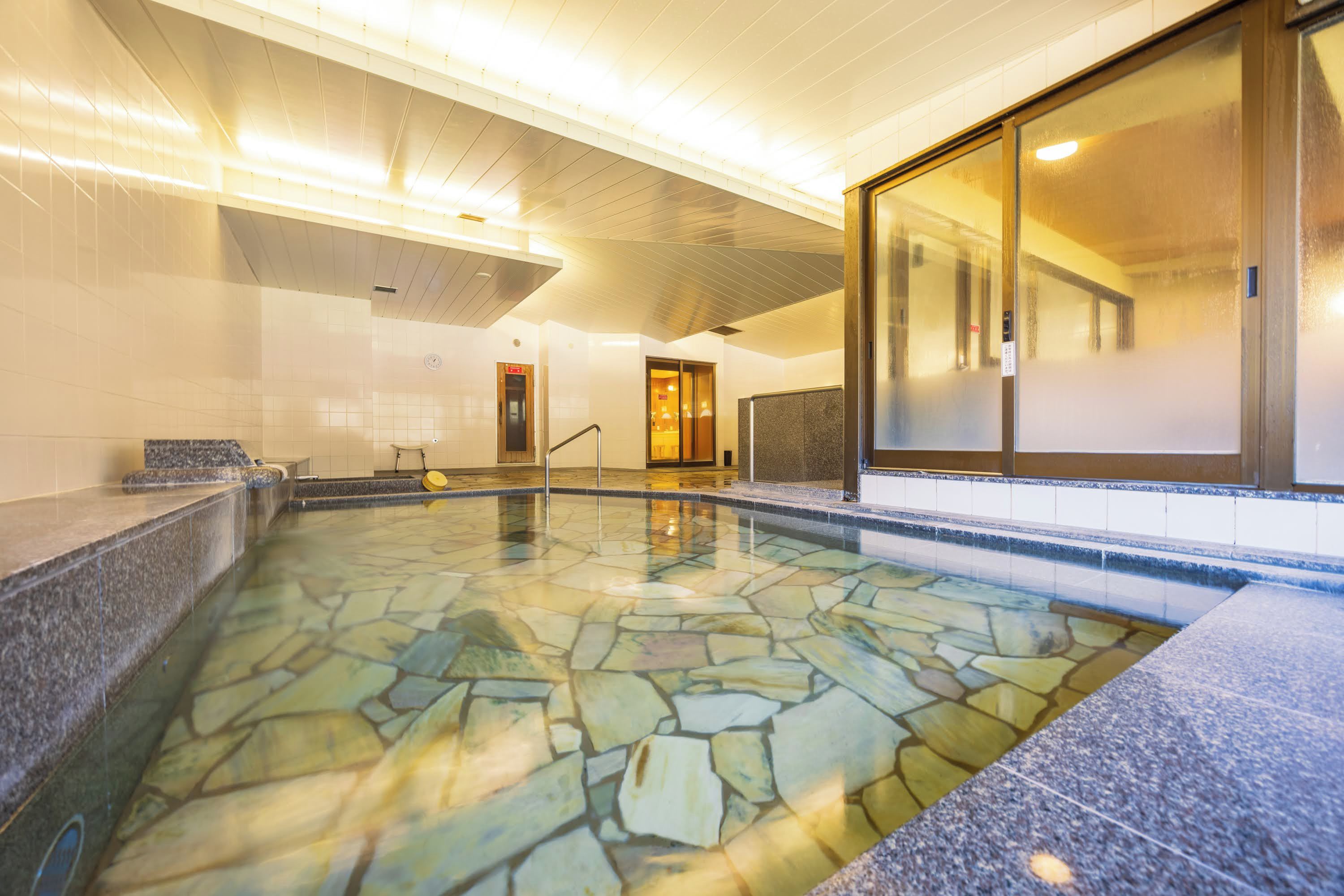 An indoor swimming pool with stone tiles, a reception area, and a glass door leading to another room.