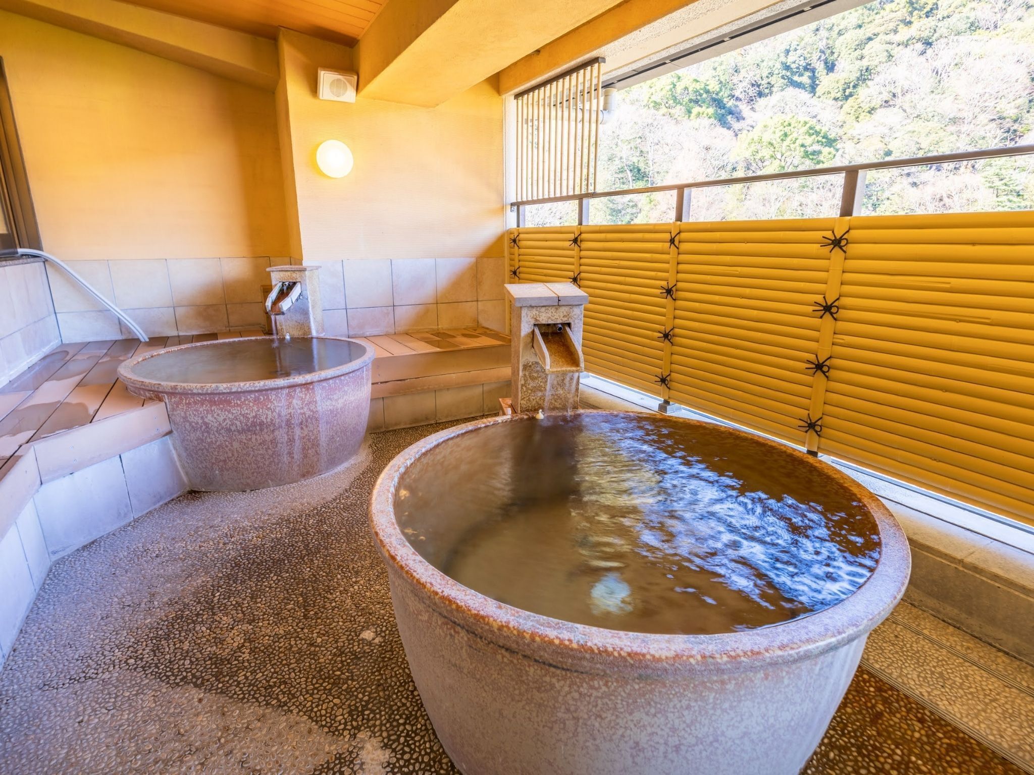 Un onsen japonais traditionnel doté de deux grandes baignoires en pierre et d’une porte coulissante en bois.