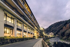 A modern hotel with multiple floors, a stone retaining wall, and a river running alongside. - Hakoneji Kaiun (Hakone)
