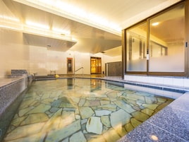 Una piscina con suelo de mosaico de piedra, un área de recepción con un banco y un amplio ventanal que da a otra habitación.