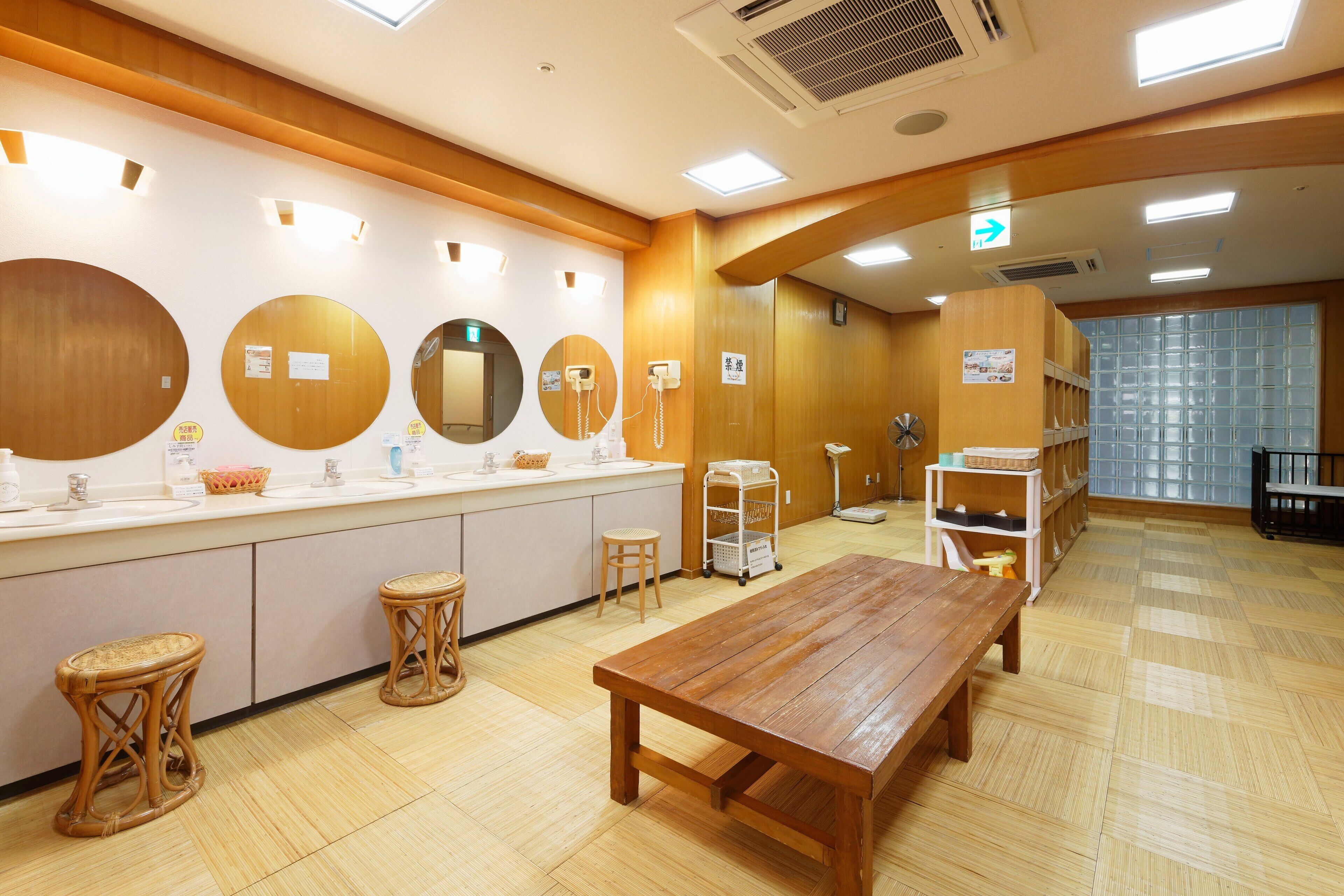 A clean, well-lit room with a wooden table and stools, a counter with a mirror, and a small cart.