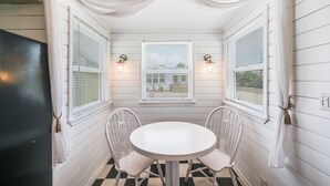 Ein Eckzimmer mit rundem Tisch und zwei Stühlen, weißen Fensterläden und Wandleuchten.