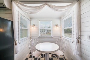 Une pièce d’angle avec une table ronde et deux chaises, des volets blancs et des lampes fixées au mur.