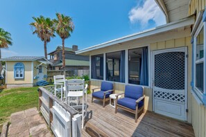 A covered outdoor deck with a seating area, a wooden fence, and a view of a house with a balcony. - Very quiet and private to rejuvenate your soul. Relax in the backyard and watch (Port Aransas)