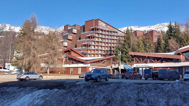 Un hotel de varios pisos con balcones, un telesilla y un paisaje montañoso.