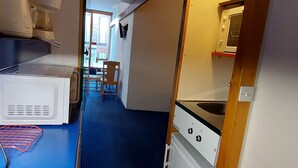 Una cocina compacta con microondas, un refrigerador pequeño y un lavamanos. Se ve un comedor con una mesa y sillas a través de una puerta abierta.