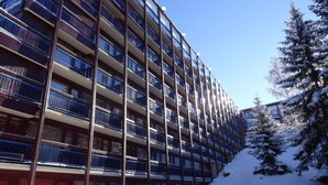 Un hotel de varios pisos con balcones, una ladera cubierta de nieve y un árbol cargado de nieve.