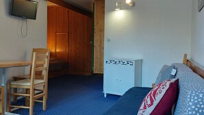 Una habitación con cama, escritorio, silla, televisor y armario.