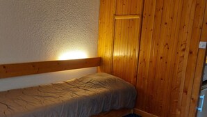 Una habitación pequeña con cama individual, cabecero de madera, piso con lunares azules y un armario de madera.