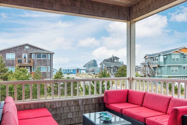 A covered balcony with red seating and a glass table, overlooking a residential area with houses and a rocky outcrop.