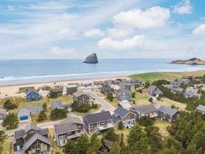 An aerial view of a coastal residential area with houses, a beach, and a rocky outcrop in the distance.