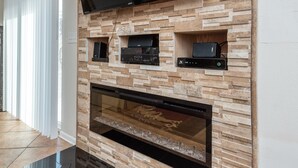 Uma sala de estar moderna com uma TV de tela plana acima de uma lareira, unidades de entretenimento embutidas e um piso preto brilhante.
