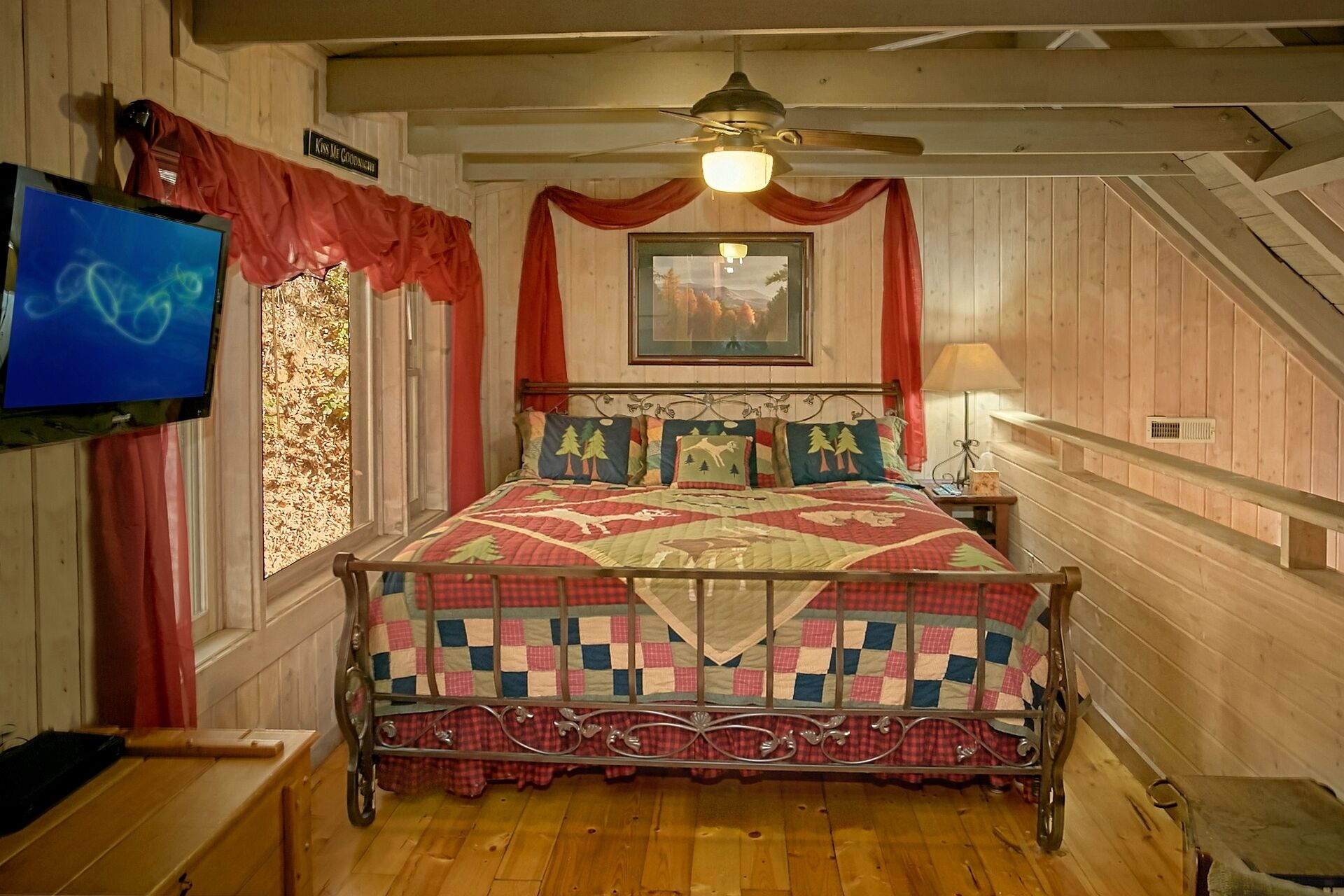 A bedroom with a metal bed frame, a ceiling fan, a television, and a framed picture on the wall.