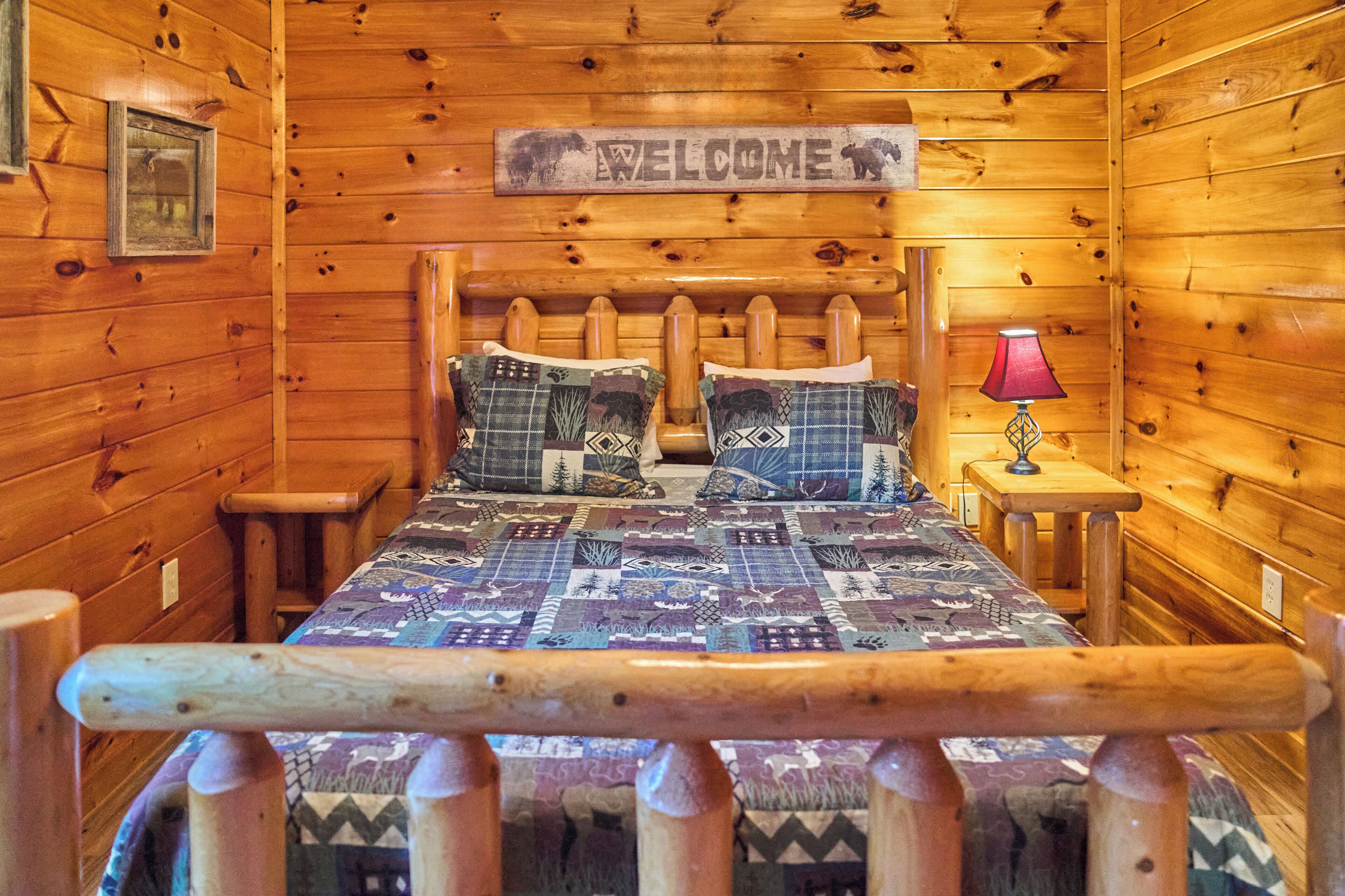 A wooden cabin room with a bed, a welcome sign, a lamp, and a framed picture on the wall.