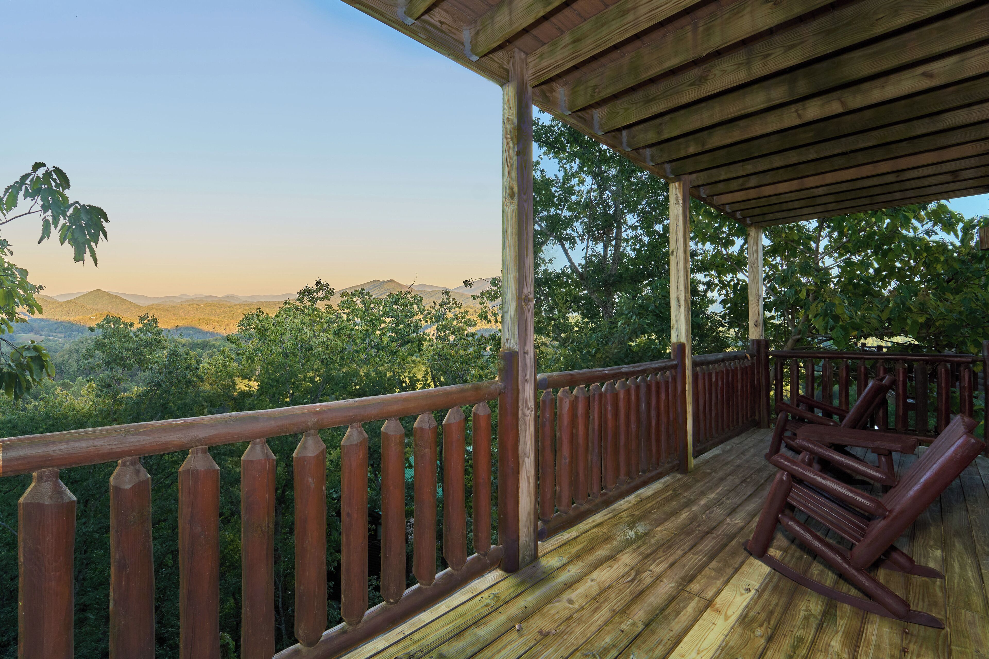 Una terraza de madera con barandilla, con vista a un área boscosa y colinas distantes.
