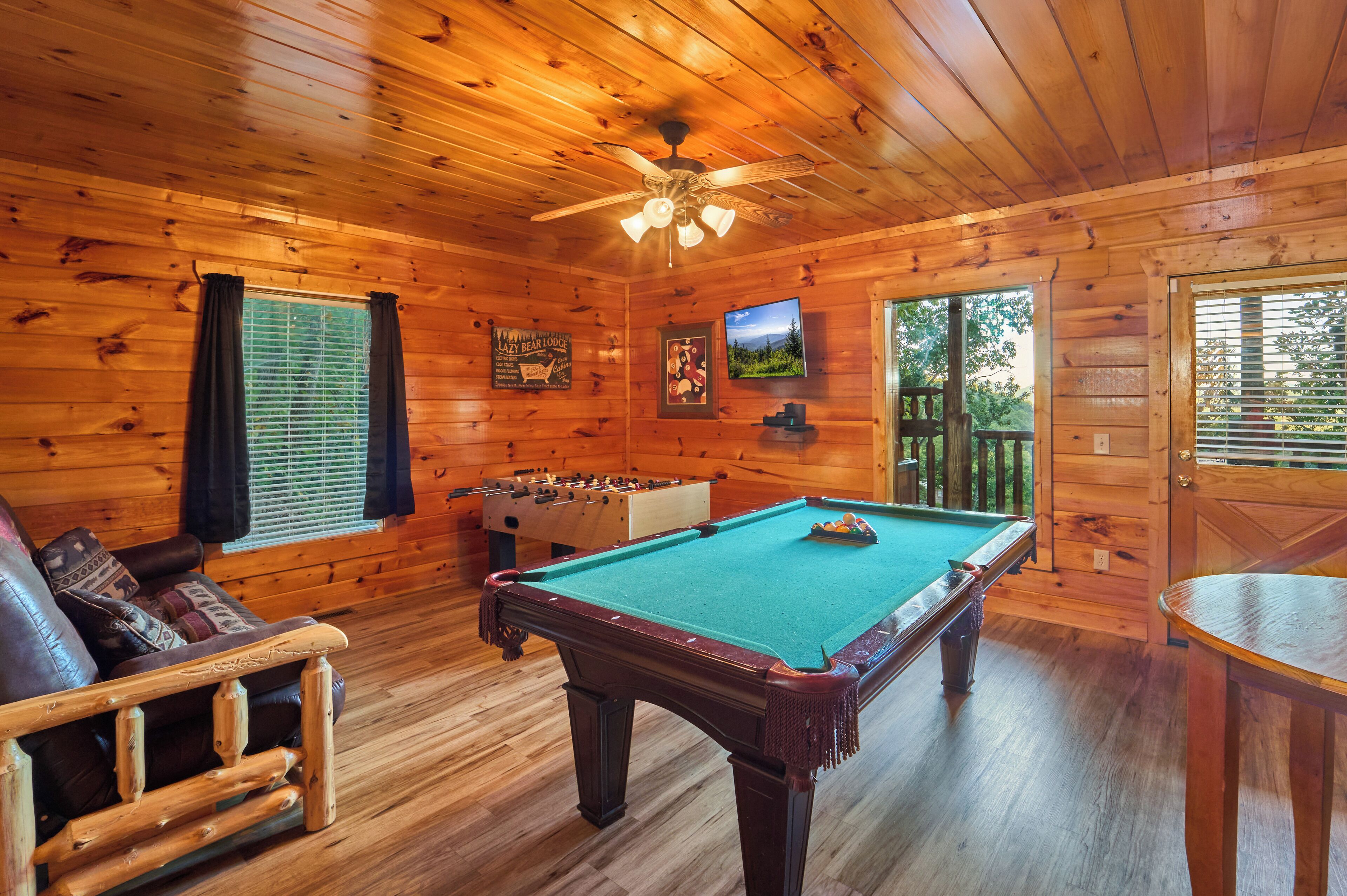 A wooden-floored room with a pool table, a sofa, and a foosball table.