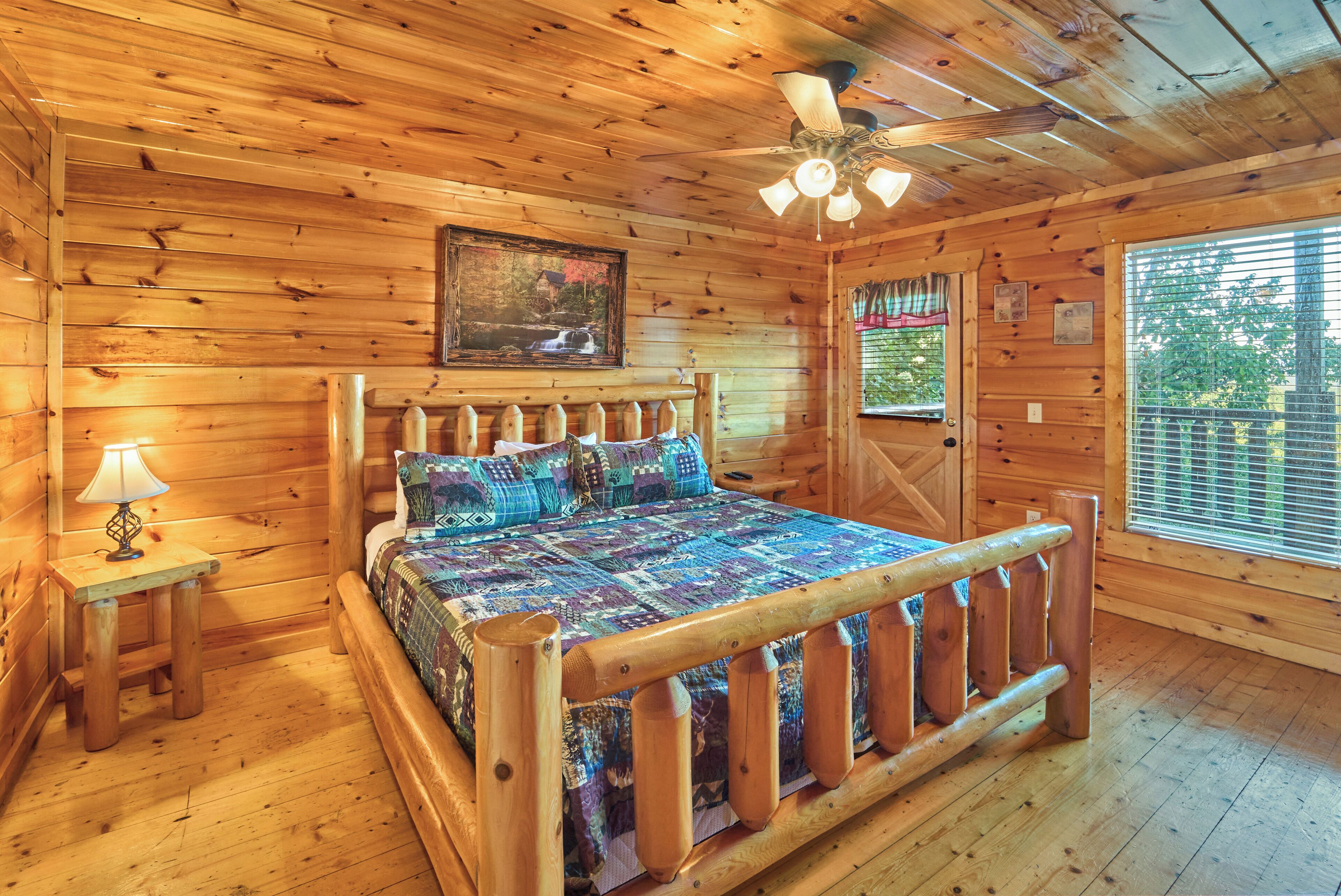 Un dormitorio de cabaña de madera con una cama, un ventilador de techo, una ventana y una puerta.
