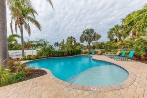 Une piscine à bord incurvé, entourée d’une terrasse en briques et de palmiers.