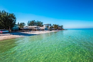 A beachfront property with clear waters, a sandy beach, and multiple houses.