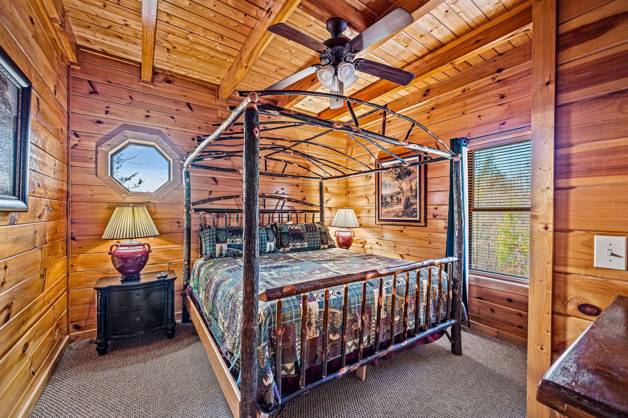 A wooden cabin bedroom with a four-poster bed, a ceiling fan, and a large window.