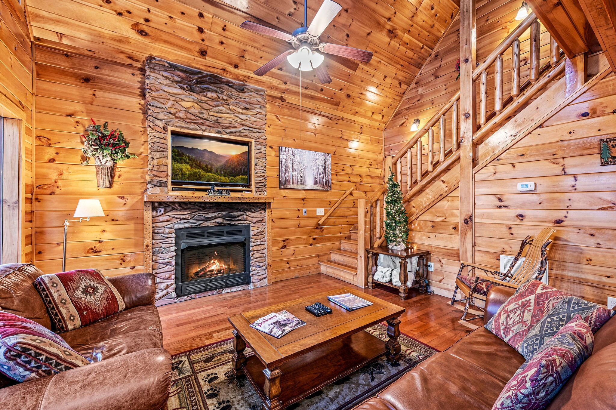 A cozy log cabin interior with a fireplace, a television, and a staircase.