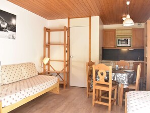 A compact living space with a sofa, dining table, chairs, a small kitchen area with a microwave, and a wooden ceiling. - Charming Studio for 4 in Méribel, Near Slopes & Shops, Balcony with Mountain Views (Méribel)