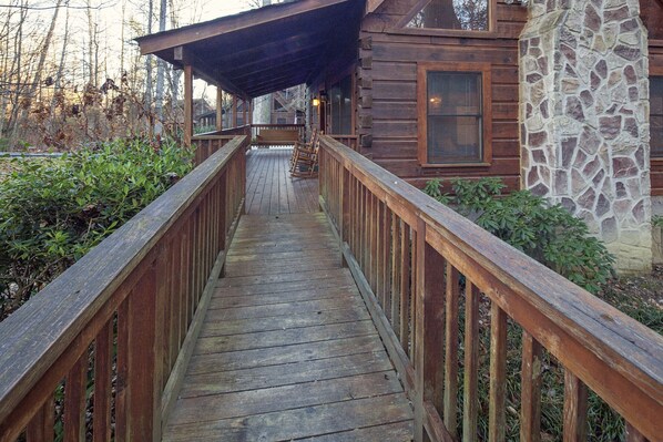 A wooden deck leading to a cabin with a stone wall and a covered porch.