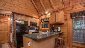 Cocina de cabaña de madera con una isla central, electrodomésticos integrados y una ventana con persianas.