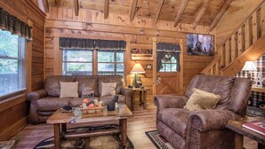 Un interior de cabaña acogedor con paredes de madera, una chimenea, un sofá y una mesita de centro.